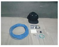 Chapéu preto com sensores e diversos componentes eletrônicos dispostos ao lado, incluindo fios, módulos e cabos, usados para montagem de um sistema assistivo.