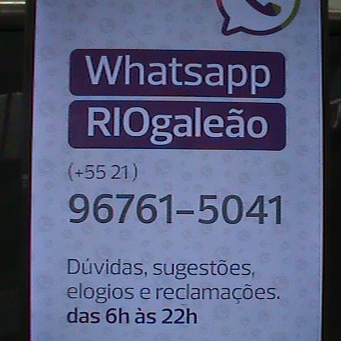 Foto de um painel do aeroporto do Galeão exibindo o número de WhatsApp disponível para atendimento. O texto informa: “WhatsApp RIOgaleão (+55 21) 96761-5041 – Dúvidas, sugestões, elogios e reclamações. Das 6h às 22h.”