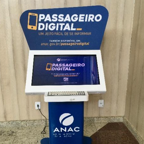Terminal do programa "Passageiro Digital" da ANAC, com tela e teclado físico integrados em estrutura azul e branca. O equipamento está posicionado em local visível e fixado ao chão, oferecendo acesso facilitado à informação sobre os direitos dos passageiros.