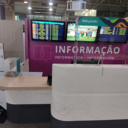 Guichê de informações do Aeroporto RIOgaleão, com altura acessível e sinalização clara da palavra "INFORMAÇÃO" em três idiomas, além de monitores com horários de voos acima do balcão.