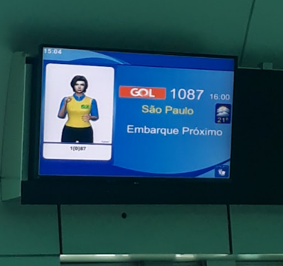 Outra imagem da mesma tela de embarque com janela de Libras, reafirmando a presença de acessibilidade em tempo real para passageiros surdos por meio da sinalização em Libras integrada à comunicação visual do aeroporto.