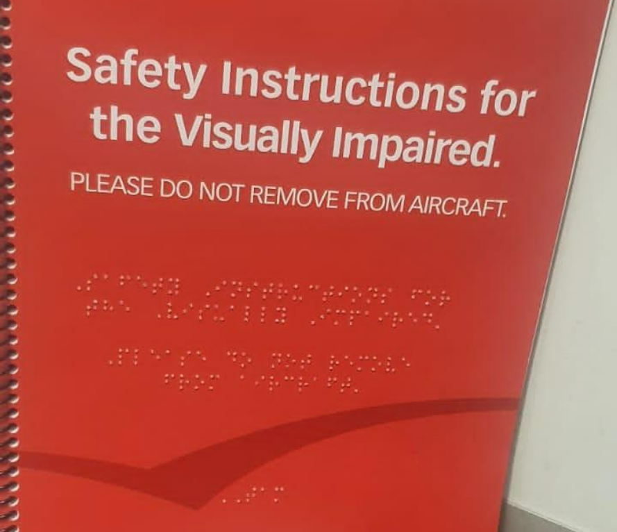Manual de segurança da aeronave com texto em inglês e transcrição em braille, específico para pessoas com deficiência visual. O aviso solicita que o material não seja removido da aeronave.