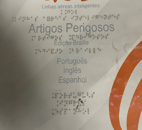 Cartaz informativo da companhia aérea Gol sobre Artigos Perigosos, com versões em Braille em três idiomas: Português, Inglês e Espanhol. O material visa orientar sobre itens proibidos no embarque.