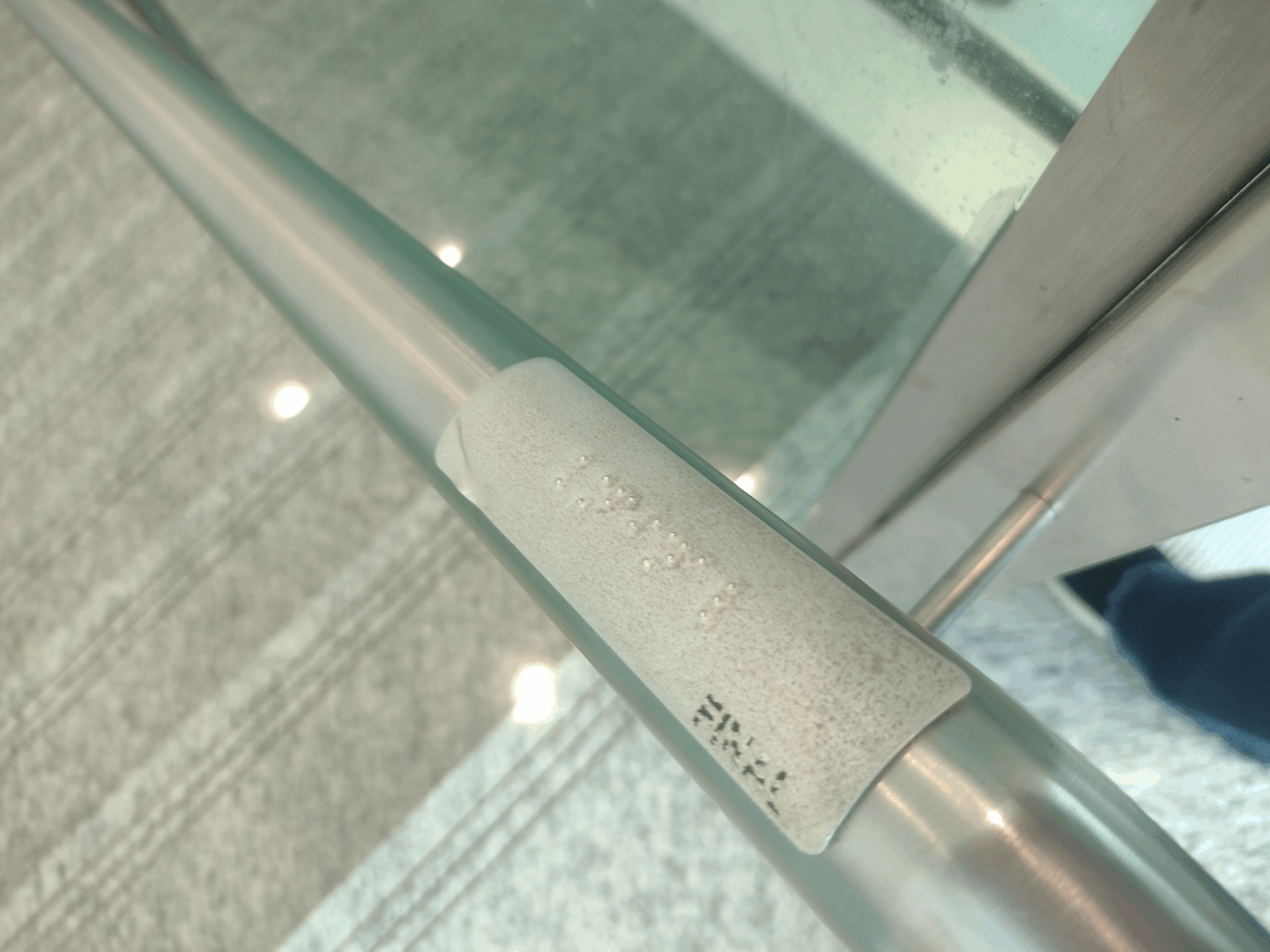 Detalhe de um corrimão de inox com uma etiqueta em relevo contendo informação em Braille para localização ou identificação do local.