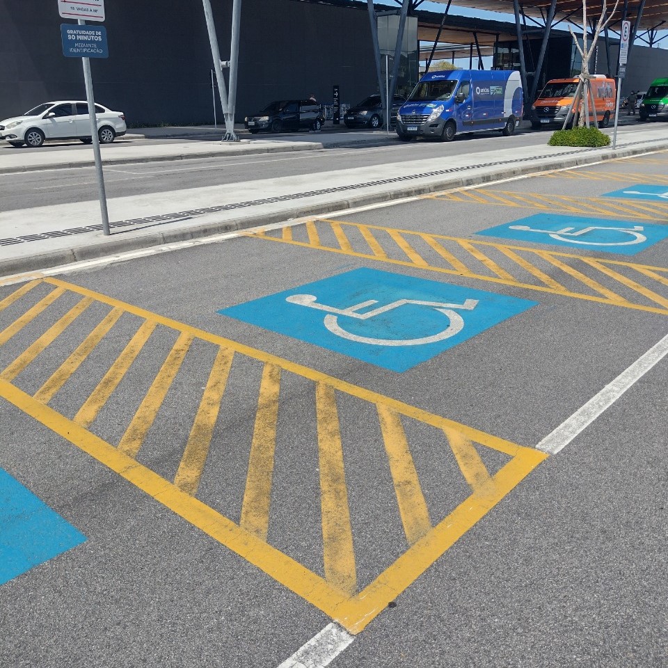 Vagas externas de estacionamento com sinalização horizontal azul e símbolo de acessibilidade, além de faixas amarelas demarcando espaço lateral para manobra de cadeiras de rodas.