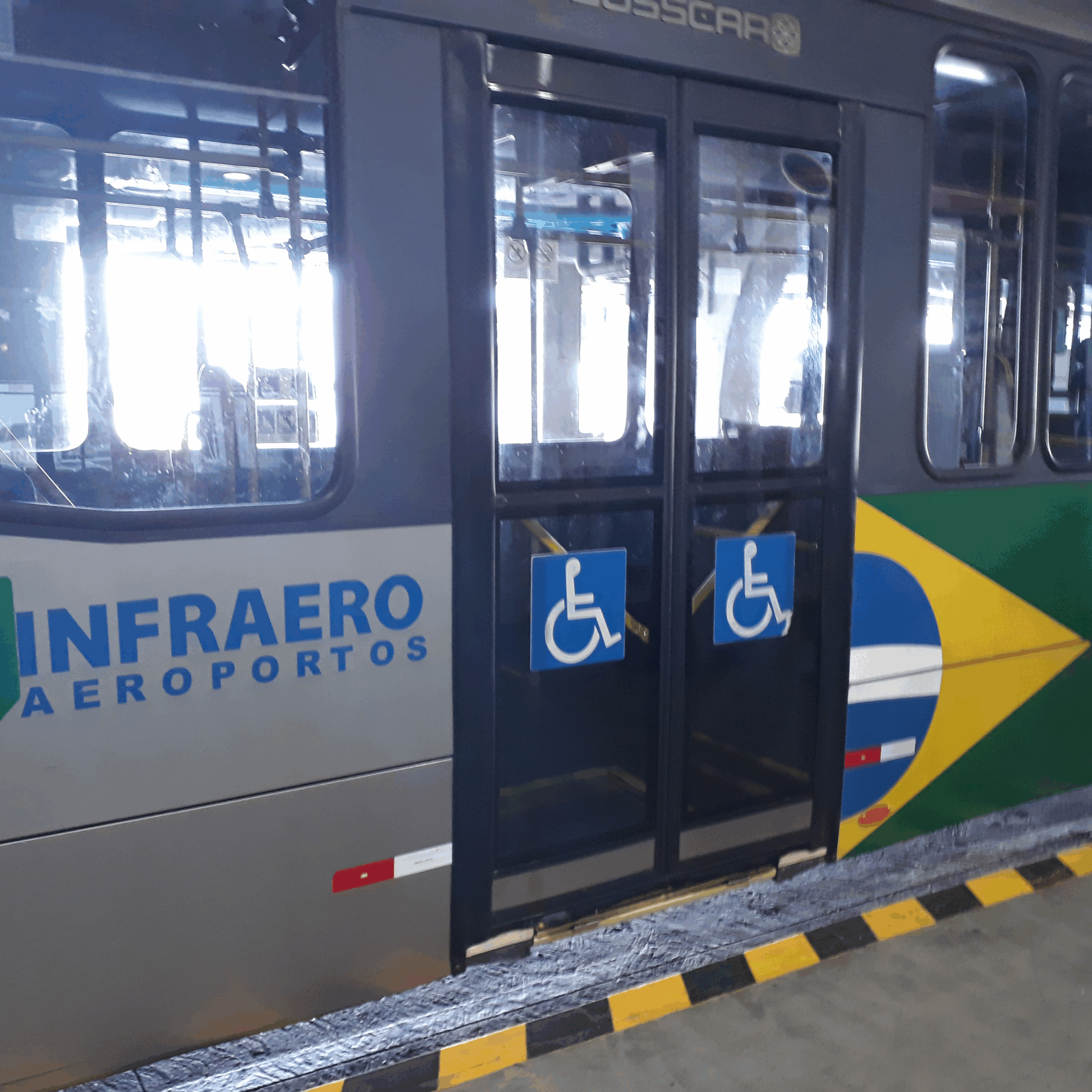 Fotografia externa de um ônibus utilizado no transporte de passageiros no aeroporto, identificado com os símbolos de acessibilidade para pessoas com deficiência física. O veículo é da Infraero e possui elevador ou rampa para cadeiras de rodas.