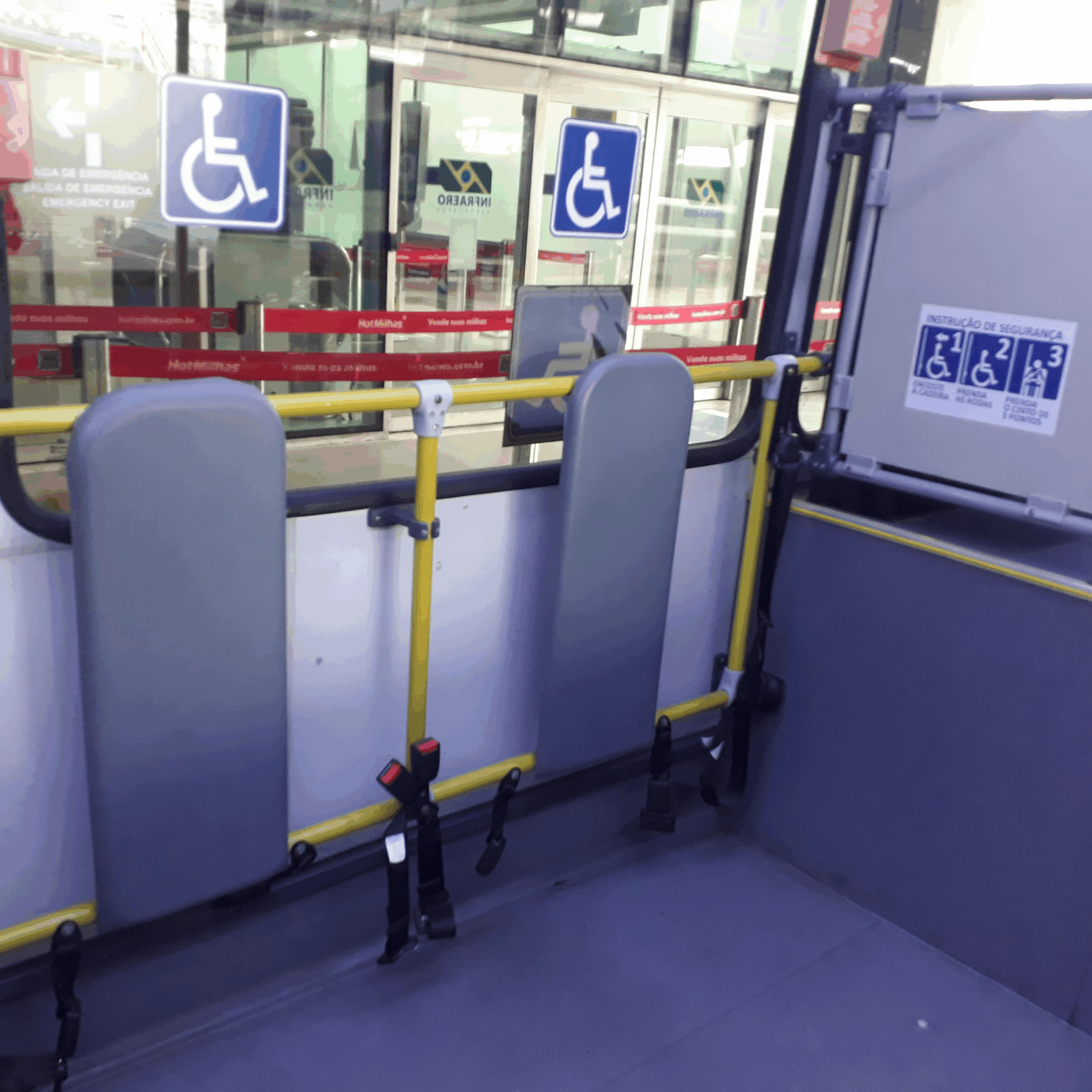 Interior do ônibus adaptado, com espaço reservado e sinalizado para cadeira de rodas. A área conta com cintos de segurança e suportes de proteção adequados.