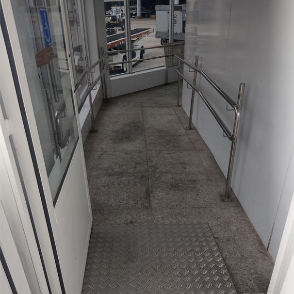Piso regular em rampa de acesso com superfície antiderrapante e corrimãos em ambos os lados, garantindo segurança e acessibilidade.