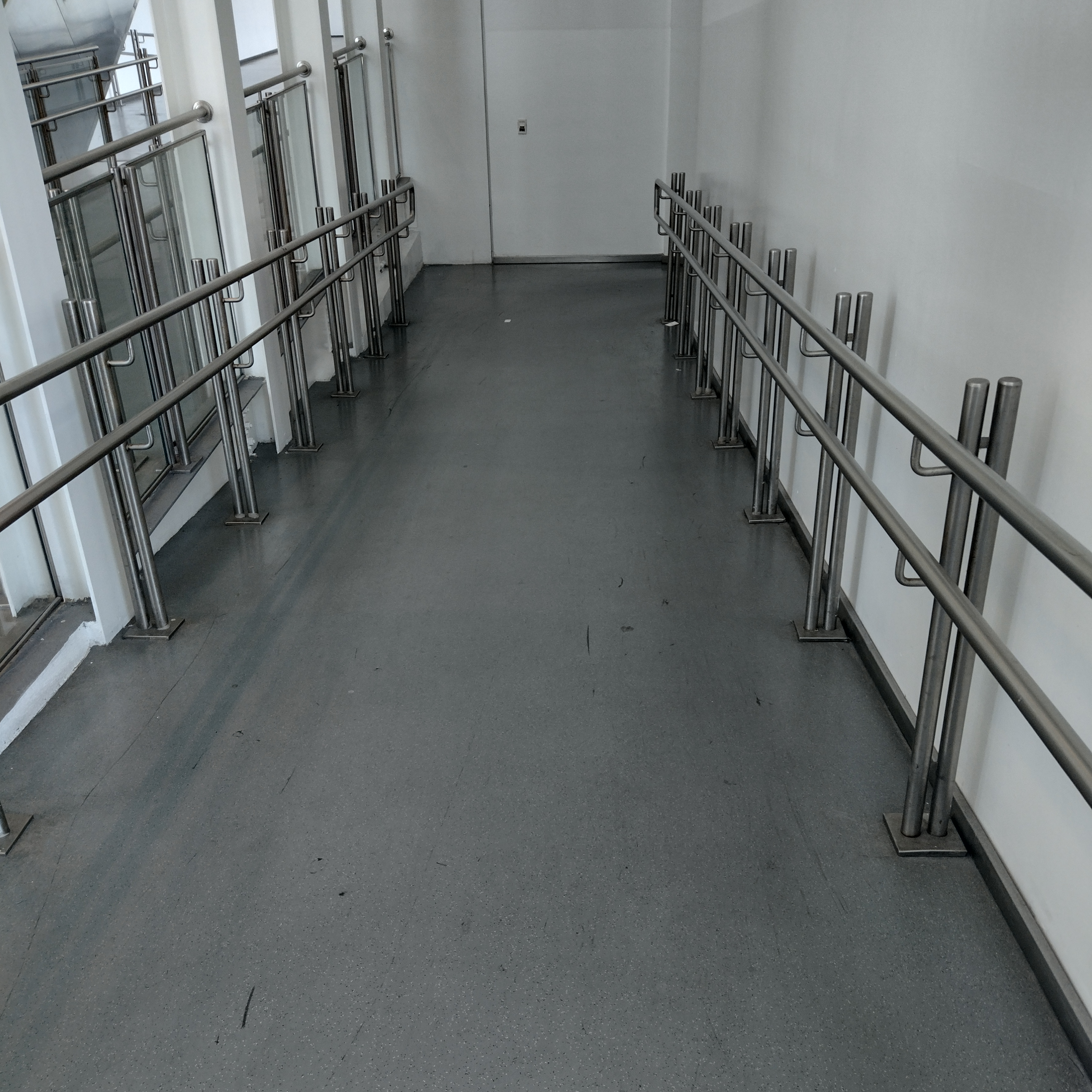 Corredor com superfície plana e contínua, largura ampla e corrimãos fixados nas laterais, sem barreiras ou obstáculos ao longo do trajeto. Adequado à circulação de cadeiras de rodas e outros dispositivos de auxílio à mobilidade.
