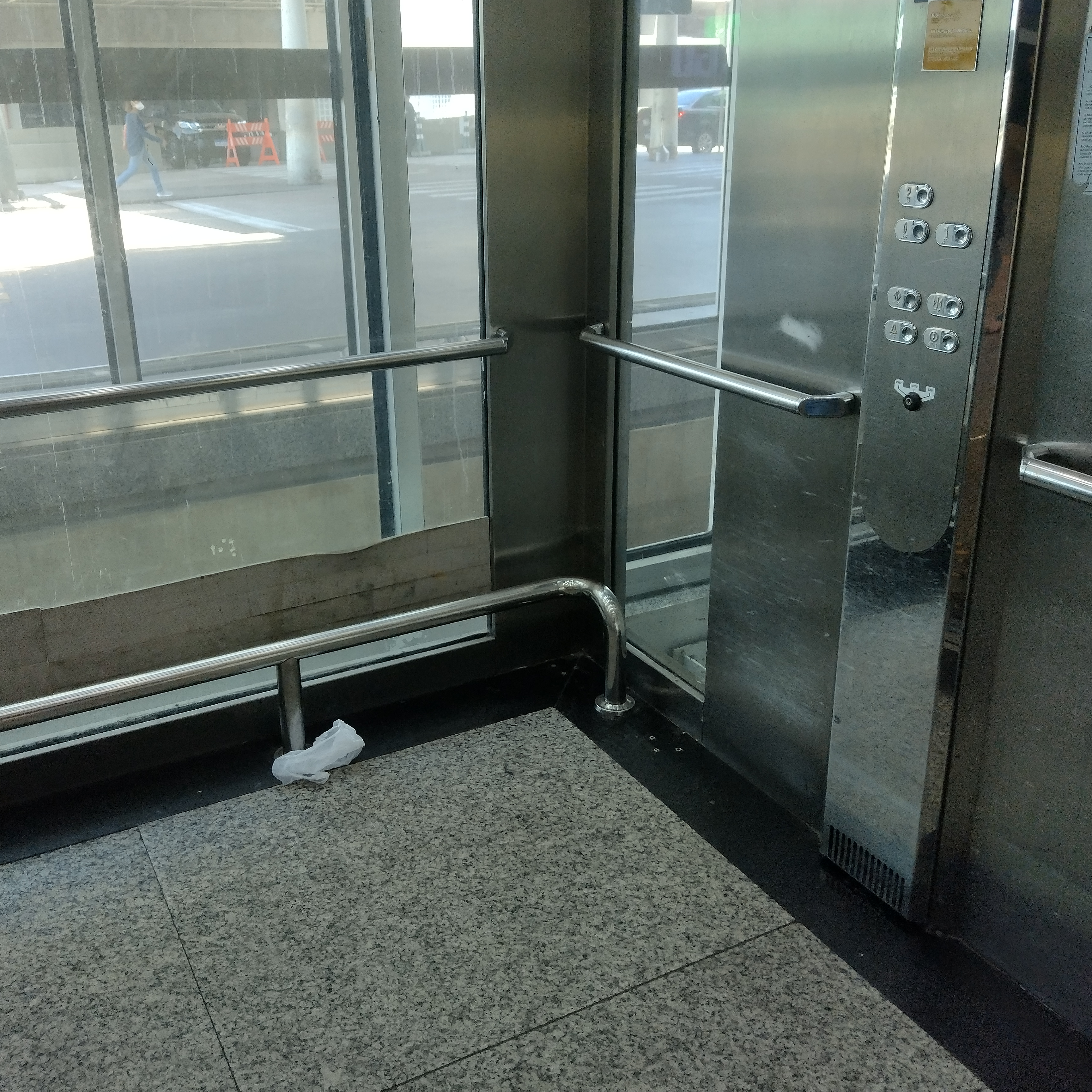 Outro exemplo de elevador acessível, com barras de apoio horizontais e verticais, incluindo uma barra mais baixa, adequada a diferentes estaturas e necessidades. O piso é plano, há piso tátil na entrada e o painel de botões está em altura acessível.