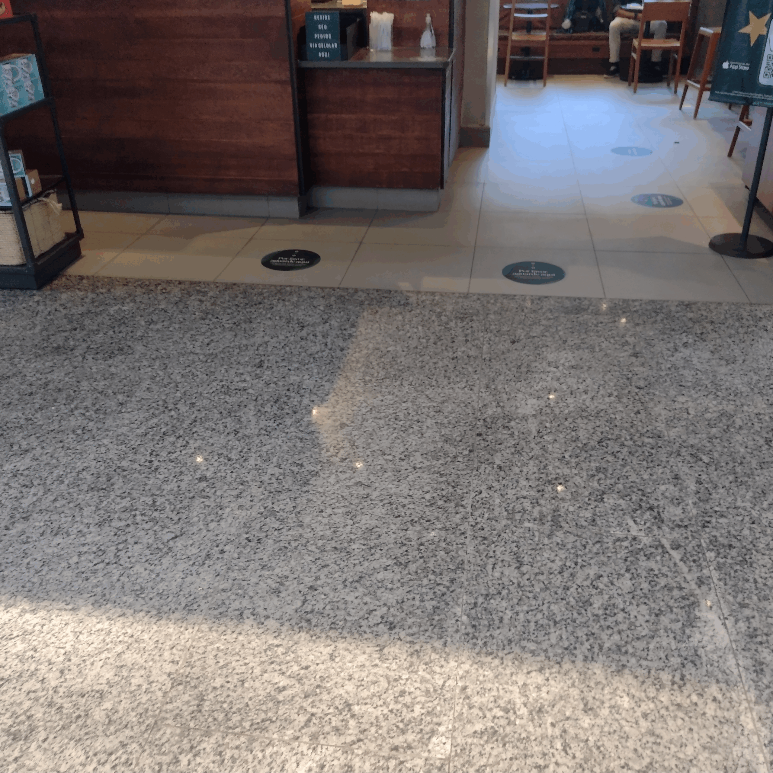 Entrada de uma loja com caminho livre e piso plano, com boa circulação para cadeiras de rodas e sinalização no chão indicando direções de atendimento.