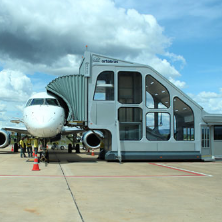 Equipamento de embarque com elevador integrado e estrutura envidraçada conectada a uma aeronave estacionada na pista.