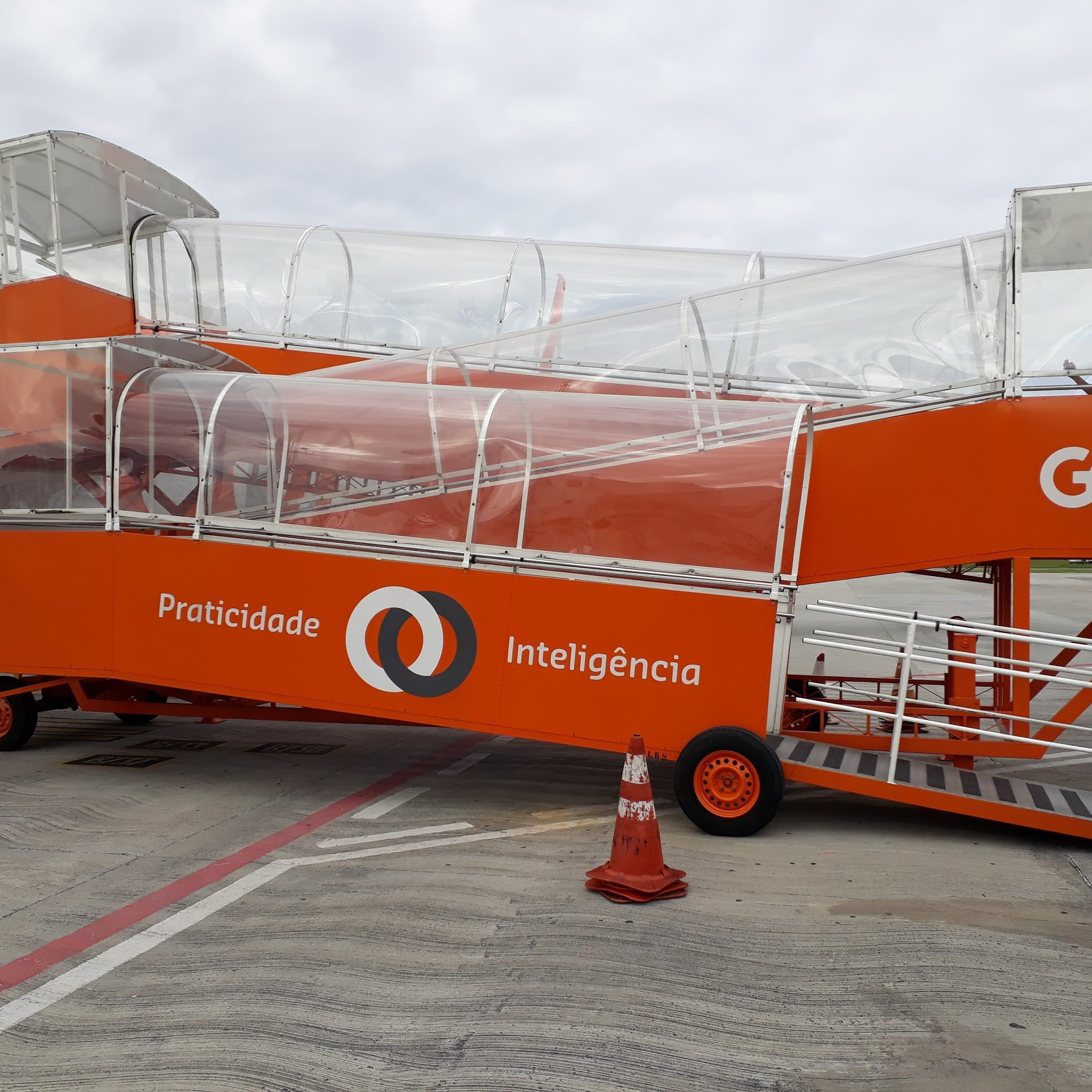 Plataforma móvel laranja com rampas cobertas e acessíveis, utilizada para embarque e desembarque remoto de passageiros, com logotipo da empresa GOL.