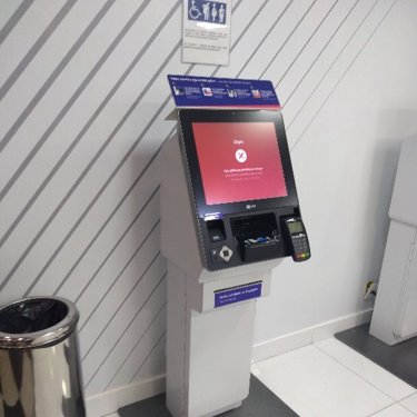 Totem de check-in da companhia aérea com altura reduzida e área sinalizada com pictogramas de acessibilidade. O equipamento possui tela inclinada, teclado numérico com contraste e terminal de pagamento acessível.