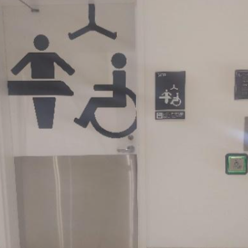 Porta de banheiro com ícones indicativos de acessibilidade e trocador, acompanhada de sinalização em Braille e botão para abertura automática da porta.